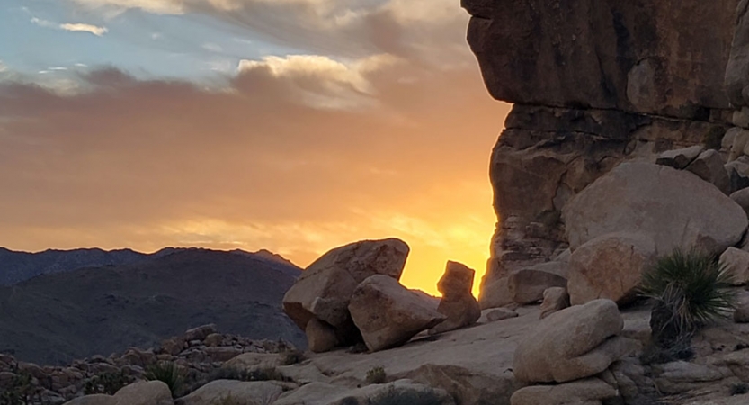the sun sets behind a large rock formation in Joshua Tree National Park
